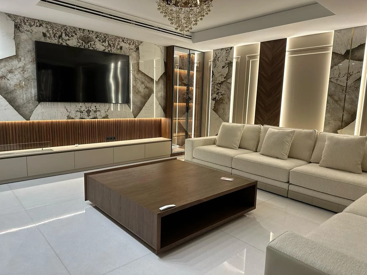 Salon aménagé par Lamouri Design : mur TV en marbre, boiseries en noyer et éclairage indirect